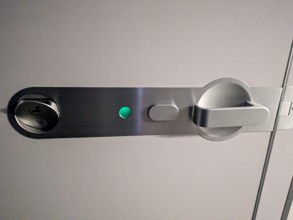 トイレのドアはノブを下に押し下げると開く。左端は灰皿。全席禁煙でも航空法によって設置が定められているⒸPen&Voyage